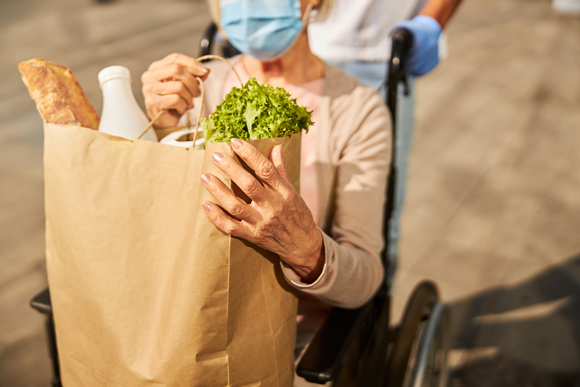 home care business in West Midlands and Walsall elderly woman in wheelchair collecting weekly shop with carer and carrying paper bag of groceries